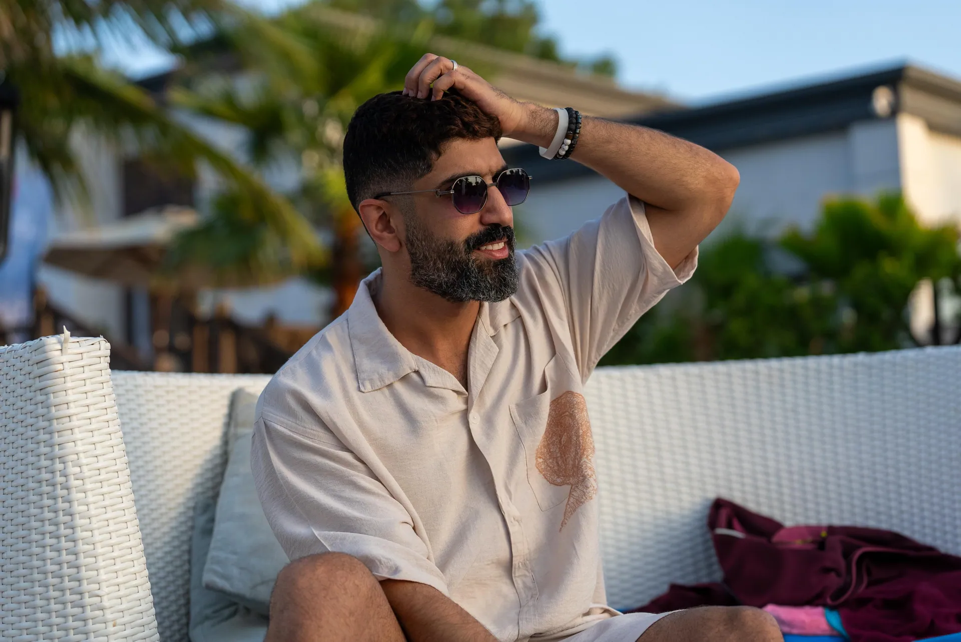 Man in a cream shirt and sunglasses on a white lounge, golden-hour resort light