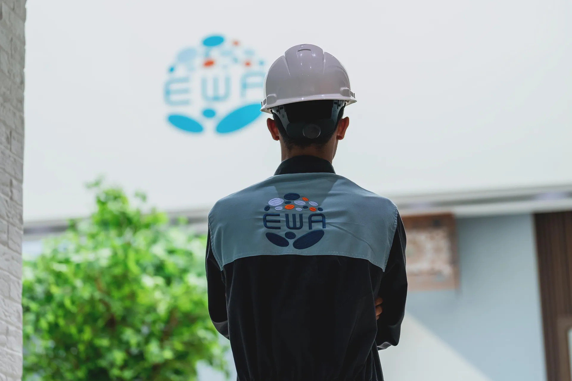 Worker in a white hard hat facing a wall-sized EWA logo