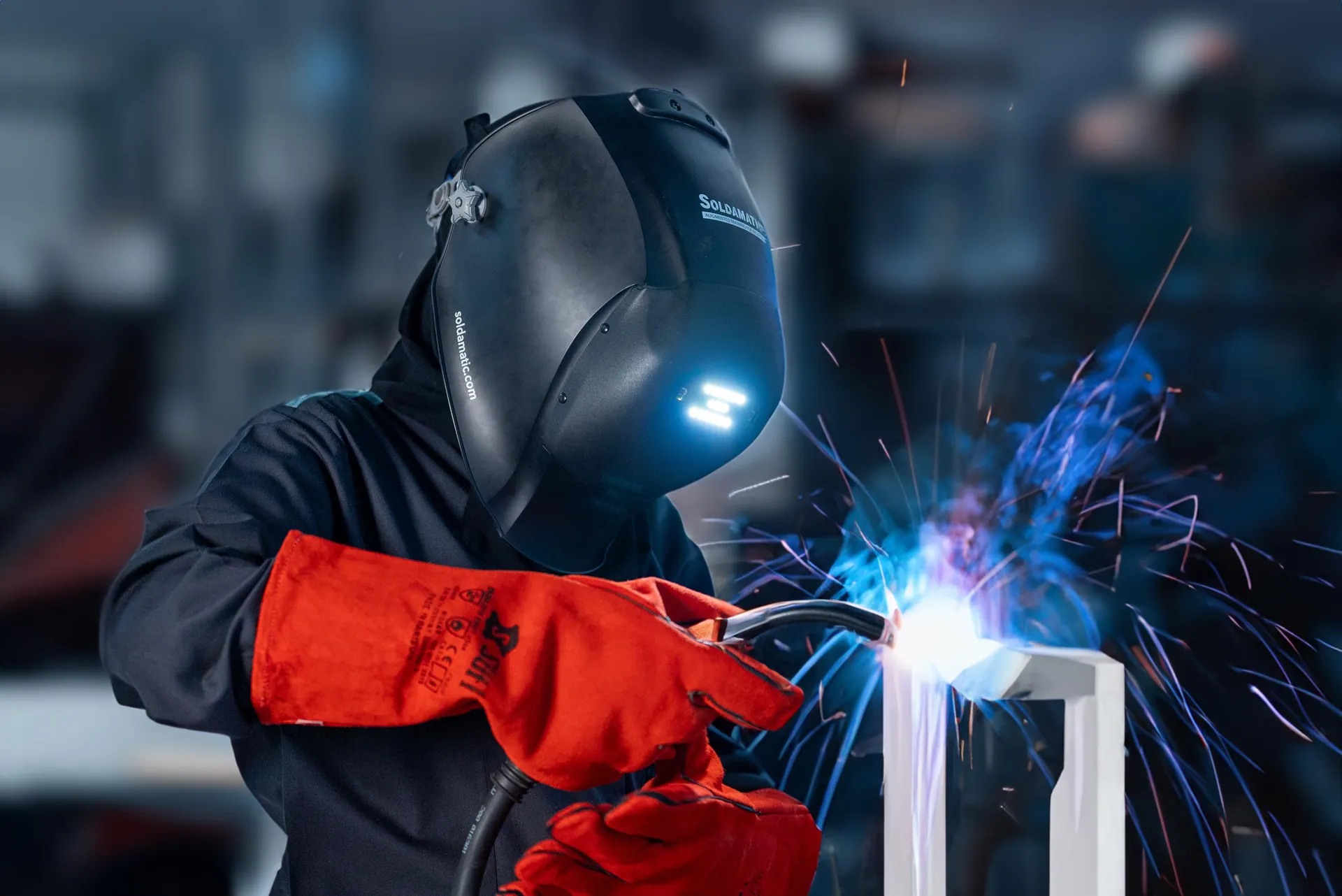 Welder in a black mask and red gloves, blue sparks flying off the seam