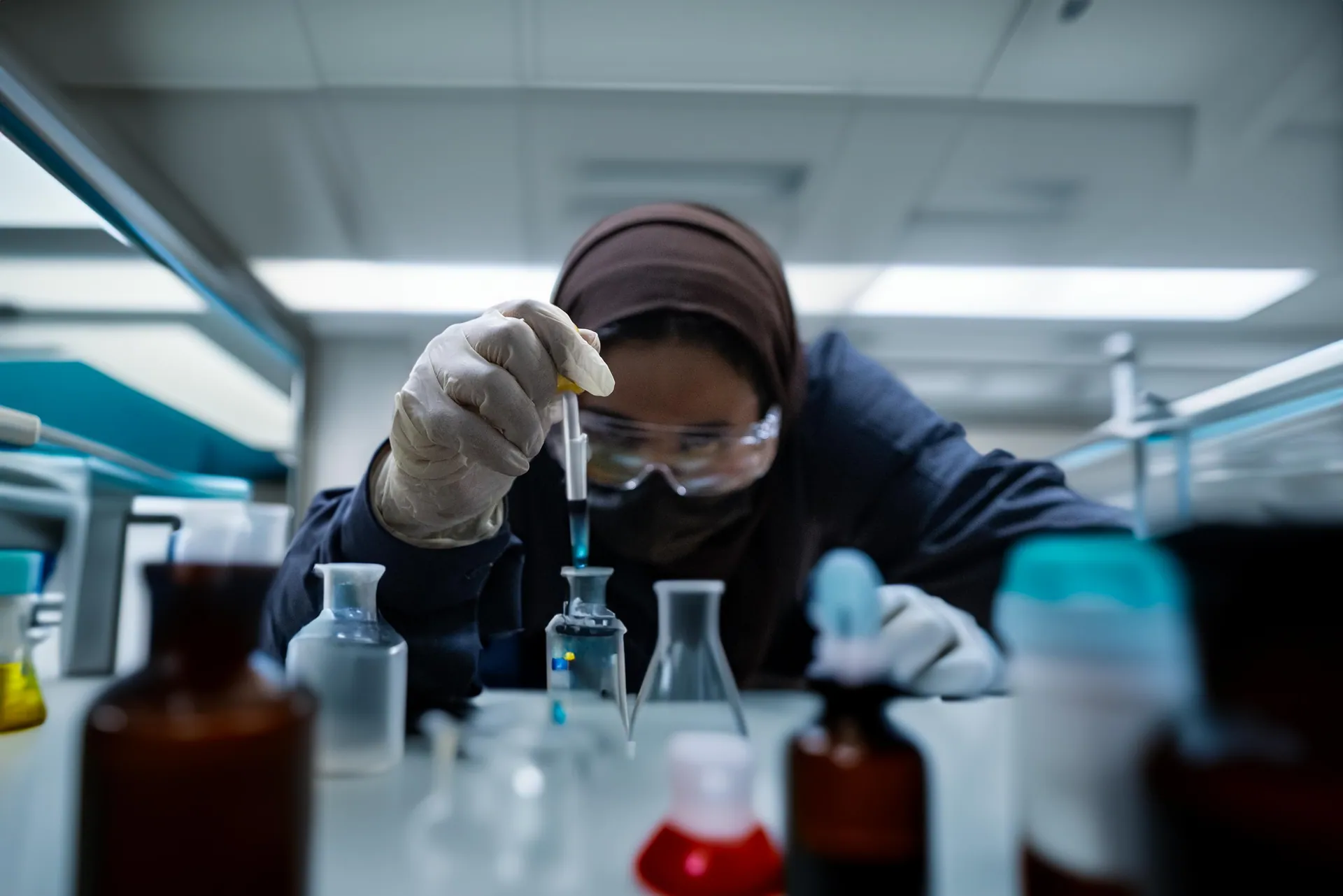 Lab chemist pipetting a blue sample between glass bottles