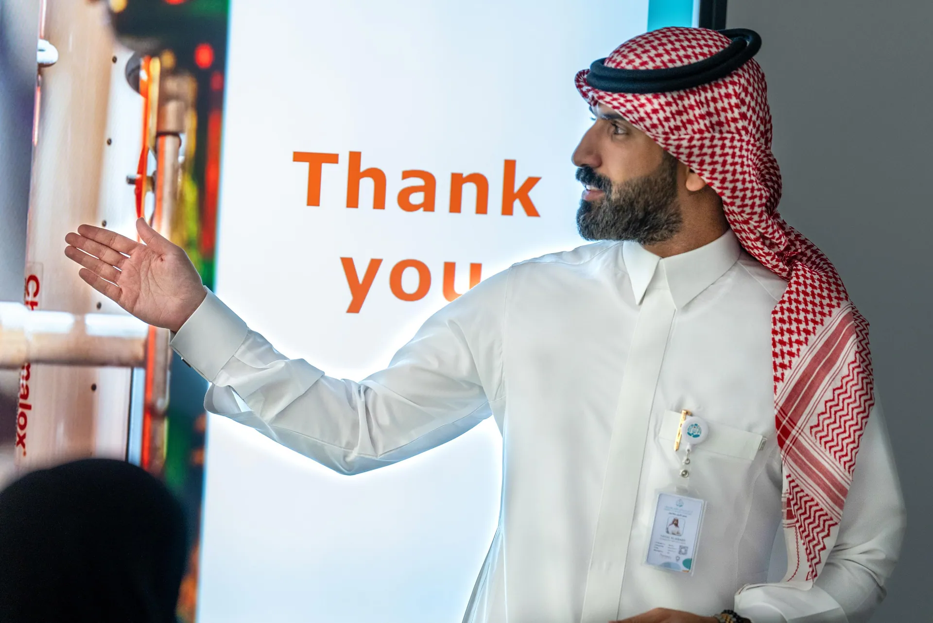 Speaker in Saudi dress presenting in front of a bright thank-you screen