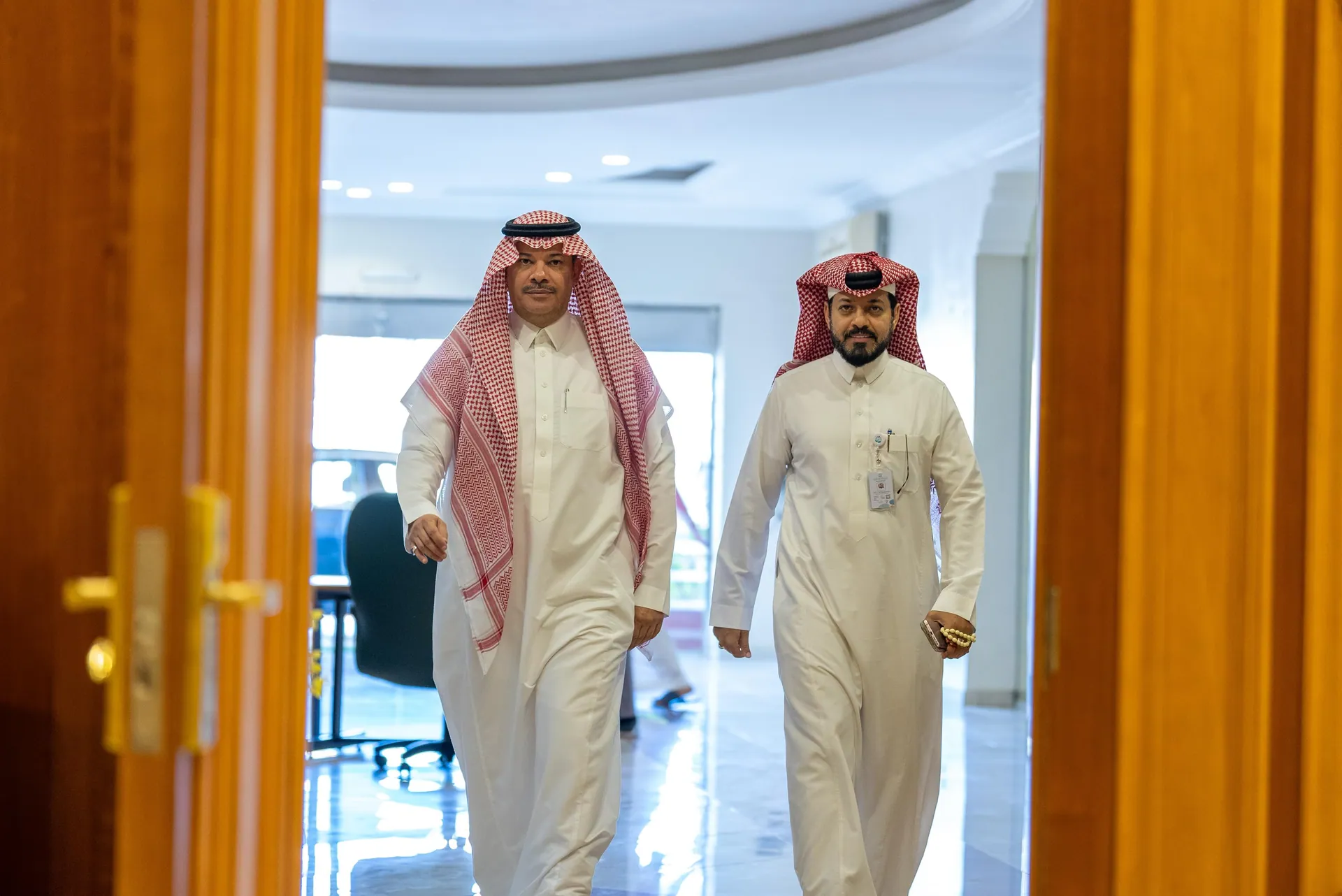 Two men in thobes walking through a bright office doorway