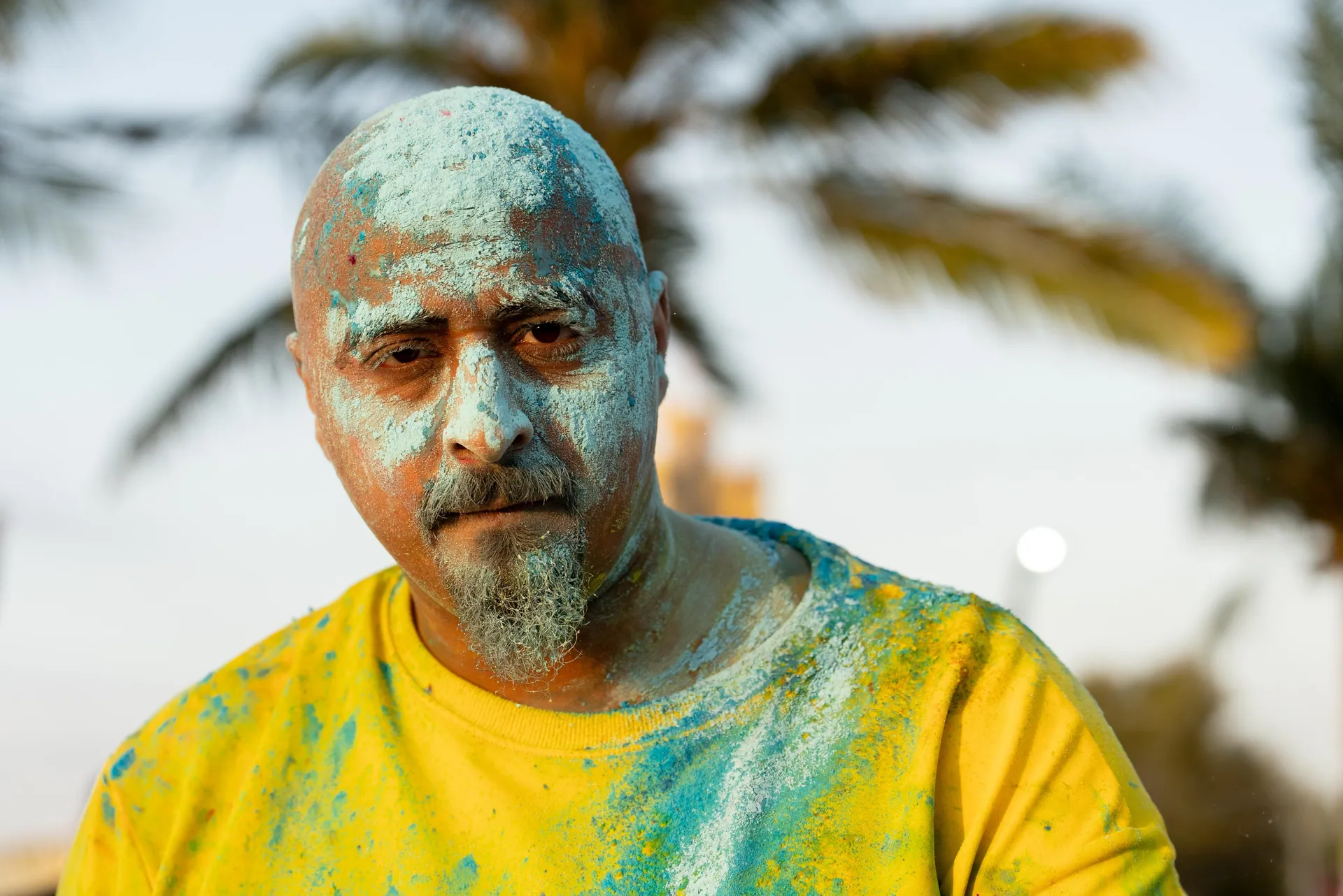 Man dusted in turquoise staring straight into the lens, palms behind