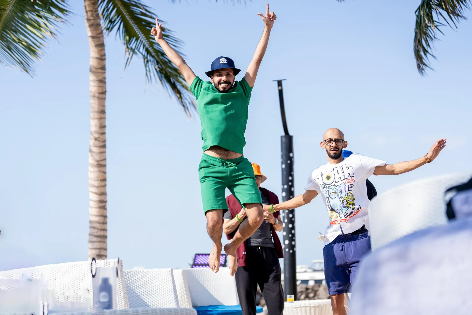 Man mid-jump with both arms up, palm trees and blue sky behind