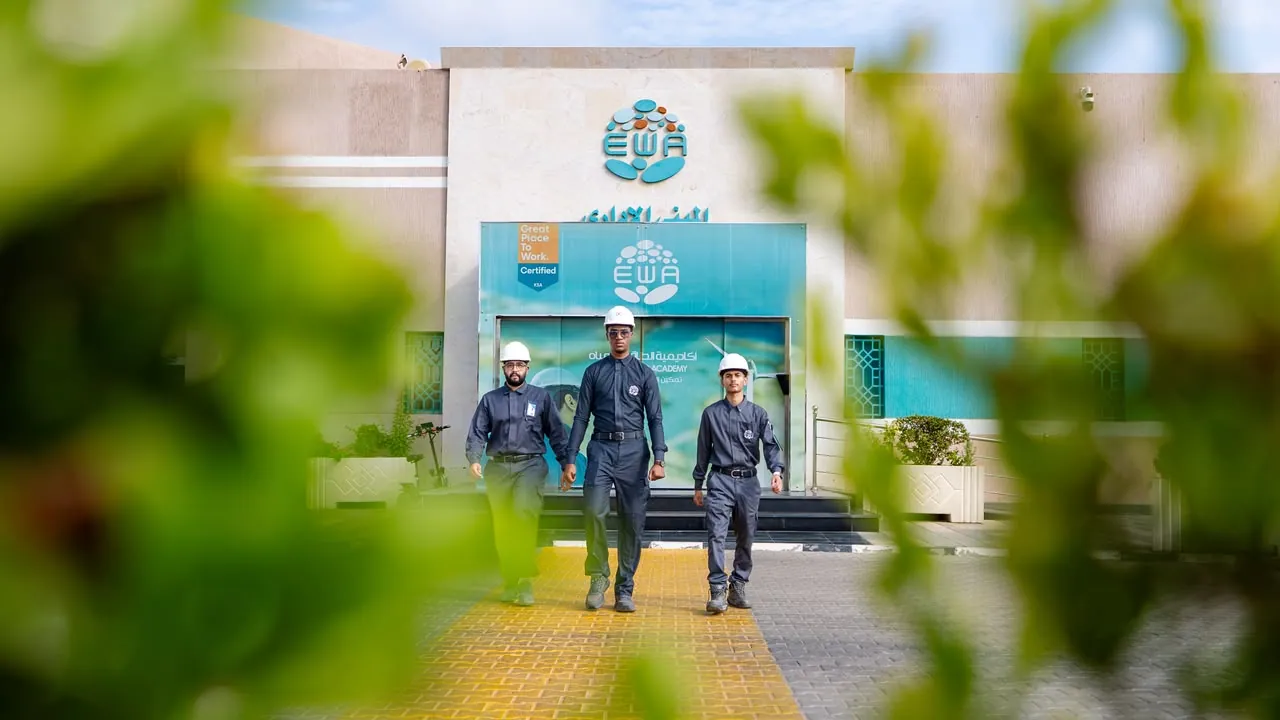 Three men in EWA coveralls and hard hats walking out of the academy, framed by blurred leaves