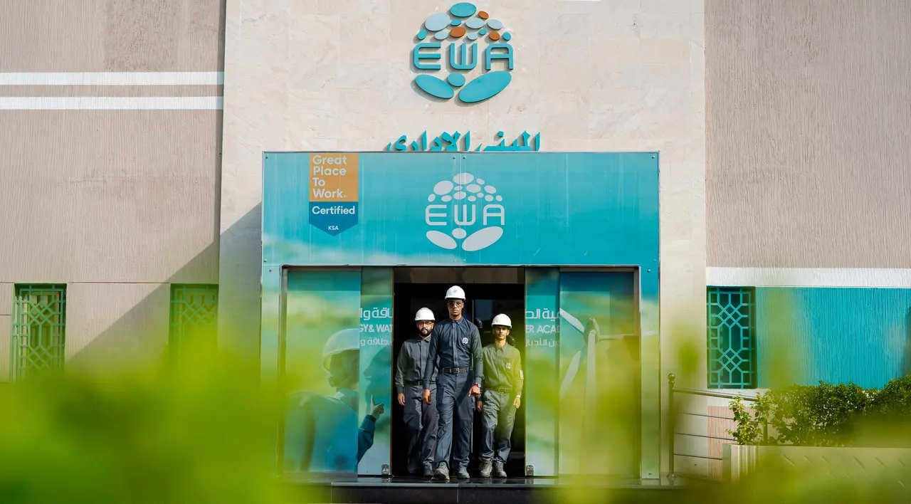 Three trainees stepping through the doors beneath the EWA sign