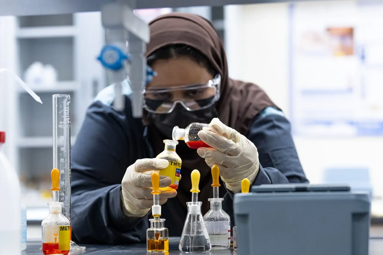 Trainee in a mask adding drops to flasks of yellow and red liquid