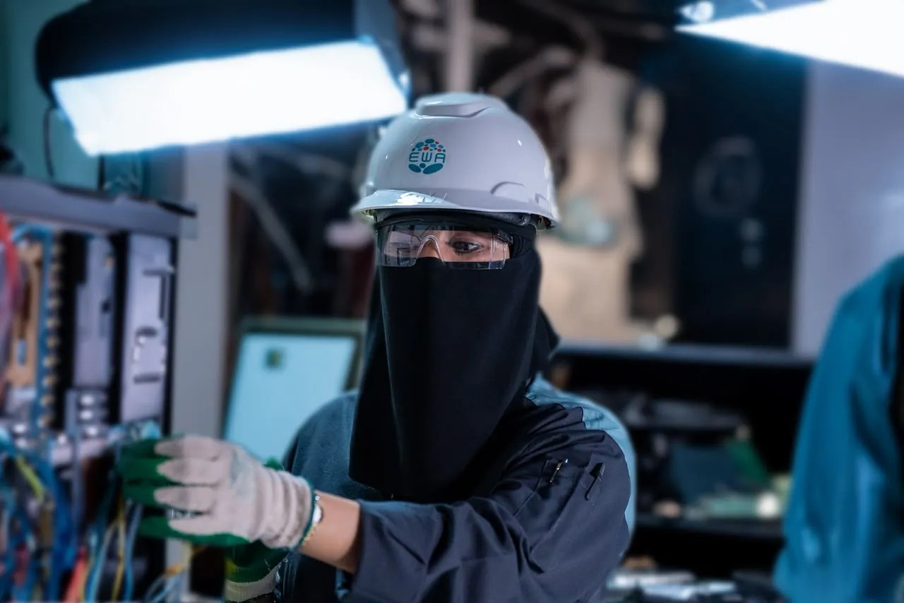 Engineer in a niqab and hard hat working on wiring under a work lamp