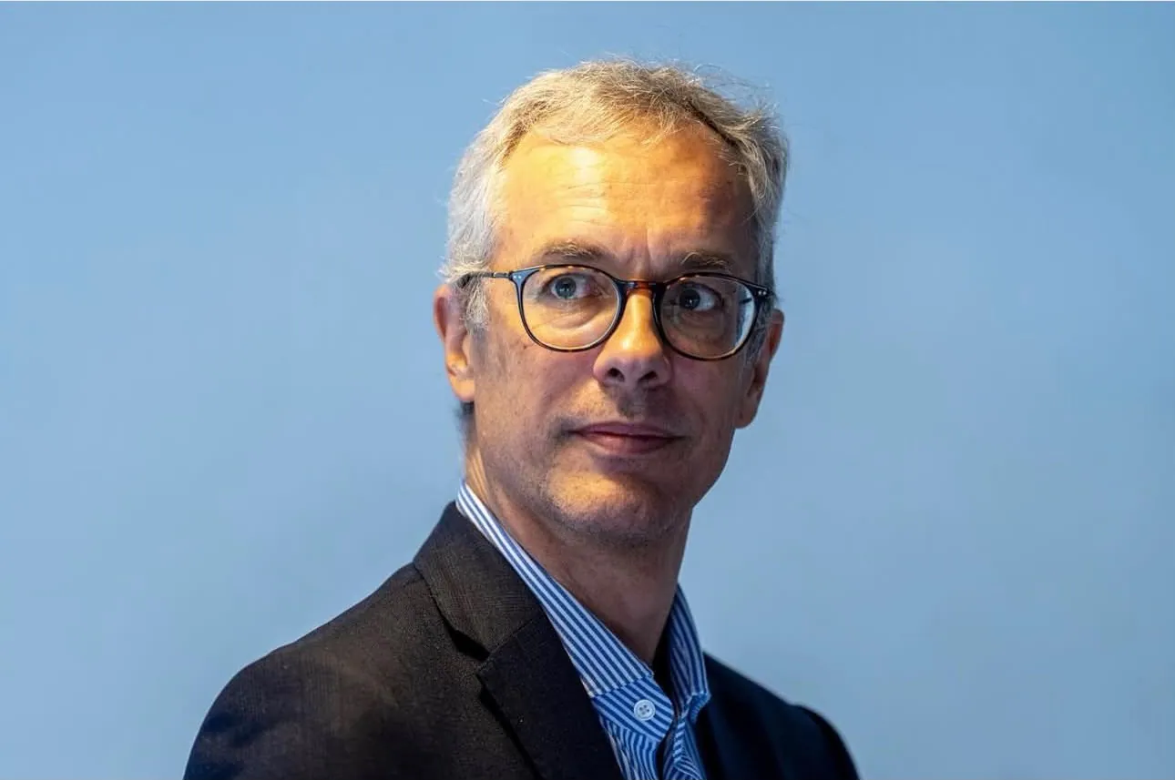 Executive in glasses and a dark jacket against a pale blue wall